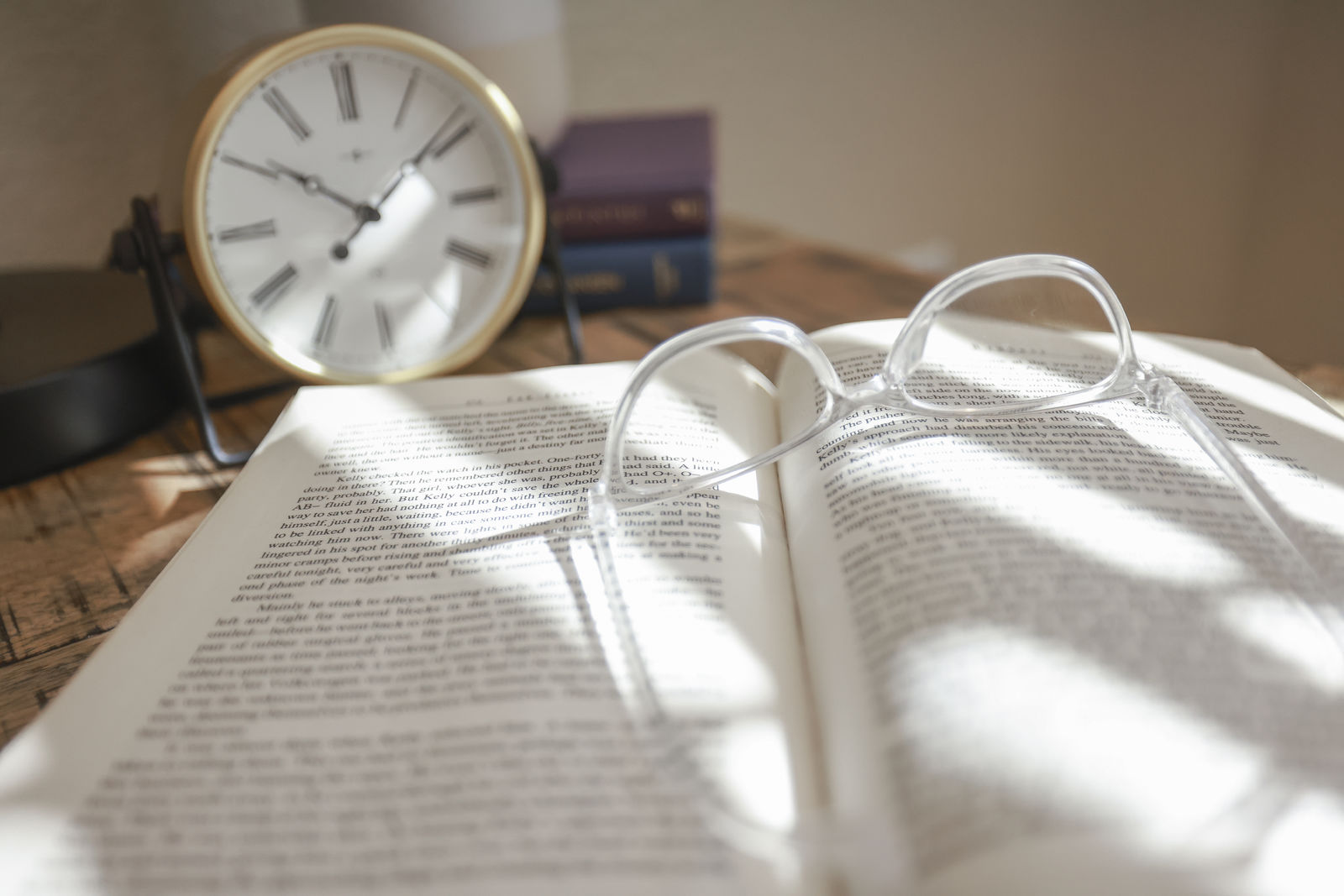 Reading glasses resting on an open book beside a table clock.