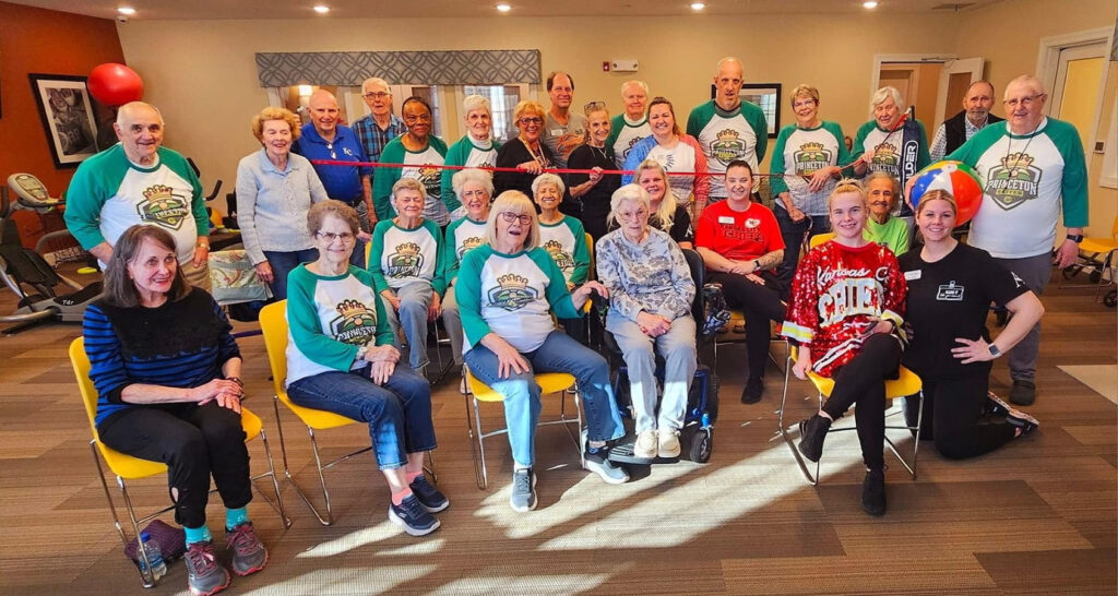 A vibrant mix of senior living residents and new employees in colorful t-shirts, playing beachball volleyball and bonding together.