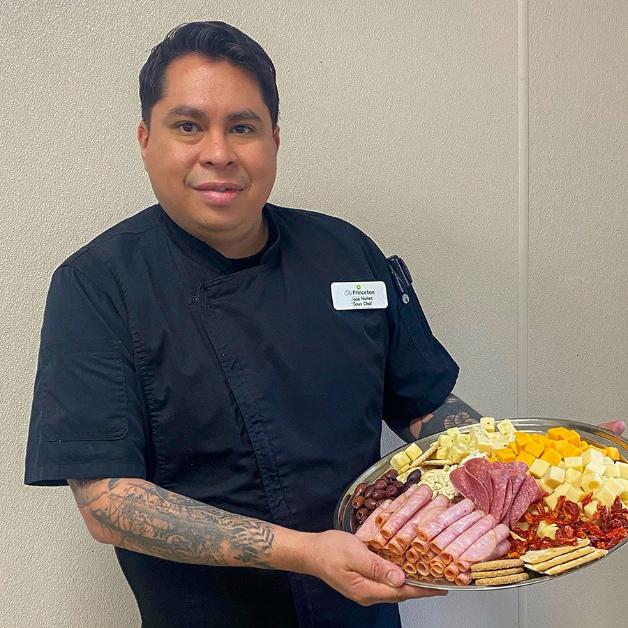 Image of Jose Nunez, a Sous Chef, in black shirt with a tray of food.