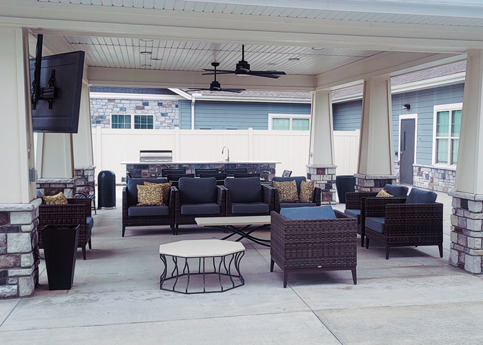 Outdoor covered patio at The Princeton Senior Living featuring cozy seating, ceiling fans, and an outdoor kitchen.