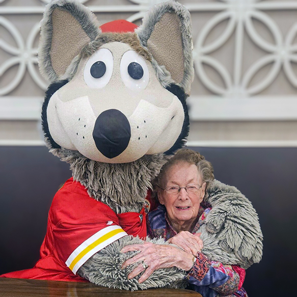 Senior resident smiles while hugging the KC Chiefs mascot, KC Wolf.