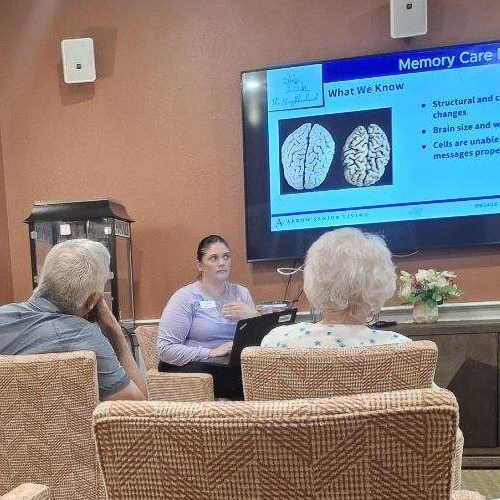 A Memory Care Director leads an educational session on brain health for senior residents, sharing insights about dementia and memory care with visuals on a screen.
