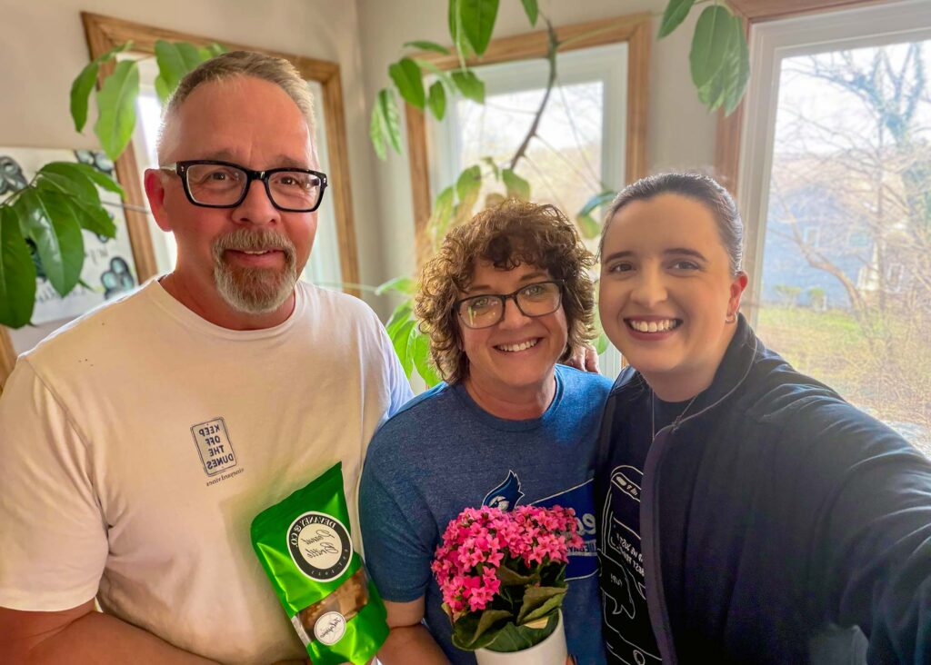 A team member from The Princeton presents a gift basket to the owners of a local business, all three smiling.