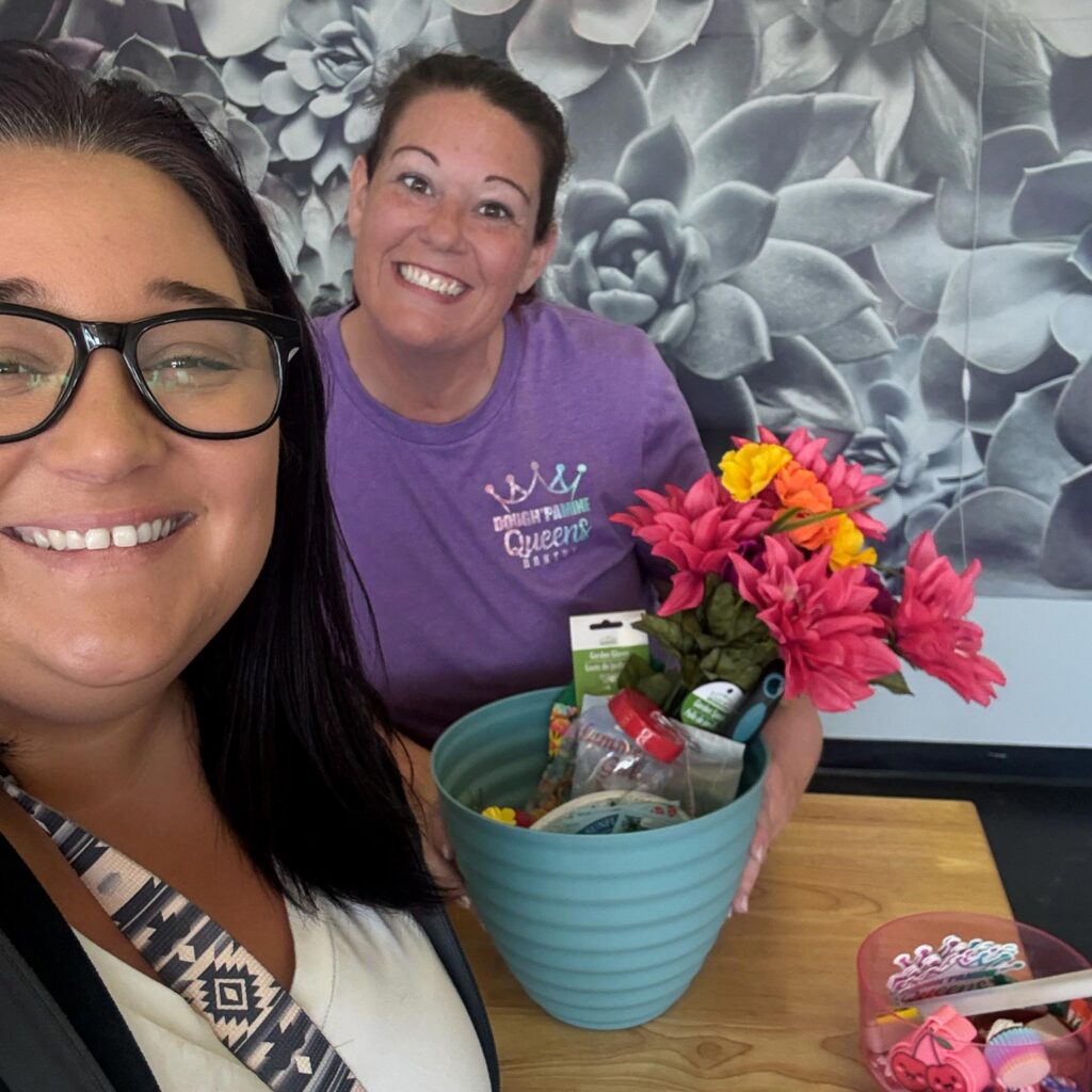 A team member from The Princeton Senior Living presents a gift basket to the owner of a local bakery, both smiling widely.