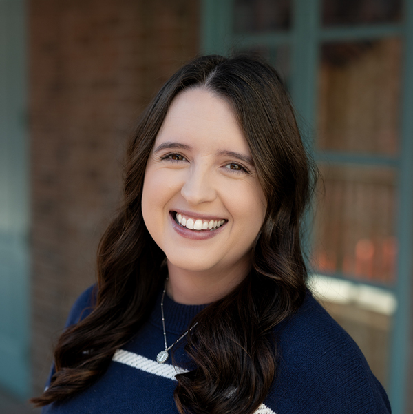 Haley Coder, Executive Director at The Princeton Senior Living, smiling in a professional headshot outdoors with dark wavy hair and a softly blurred brick and window background.