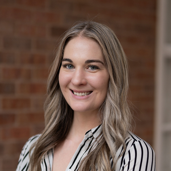 Kelsey Donyina, Memory Care Director at The Princeton Senior Living, smiling in a professional headshot with long wavy blonde hair, a striped blouse, and a softly blurred brick background.