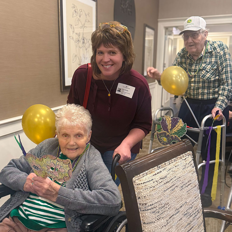 Senior residents smile alongside a loved one, holding balloons during a community event.