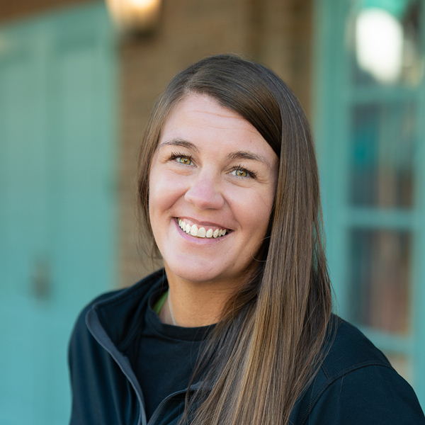 Nicole Hensley, Wellness Director at The Princeton Senior Living, smiling in a professional headshot, wearing a black top, with a softly blurred outdoor background featuring teal doors and window details.