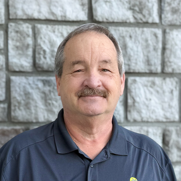 Tony Dudley, Plant Operations Director at The Princeton Senior Living, smiling in a professional headshot with a gray mustache, short salt-and-pepper hair, and a light stone wall background.
