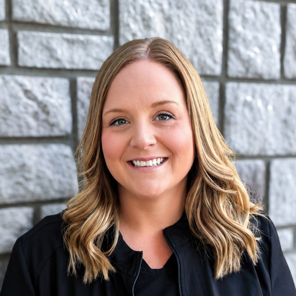 Keely Casey, Wellness Director at The Princeton Senior Living, smiling in a professional headshot with shoulder-length wavy blonde hair, a black top, and a light gray stone wall background.