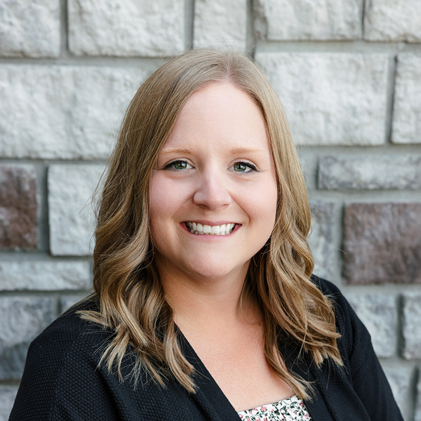 Keely Casey, Wellness Director at The Princeton Senior Living, smiling in a professional headshot with shoulder-length wavy blonde hair, a black cardigan, and a gray stone wall background.